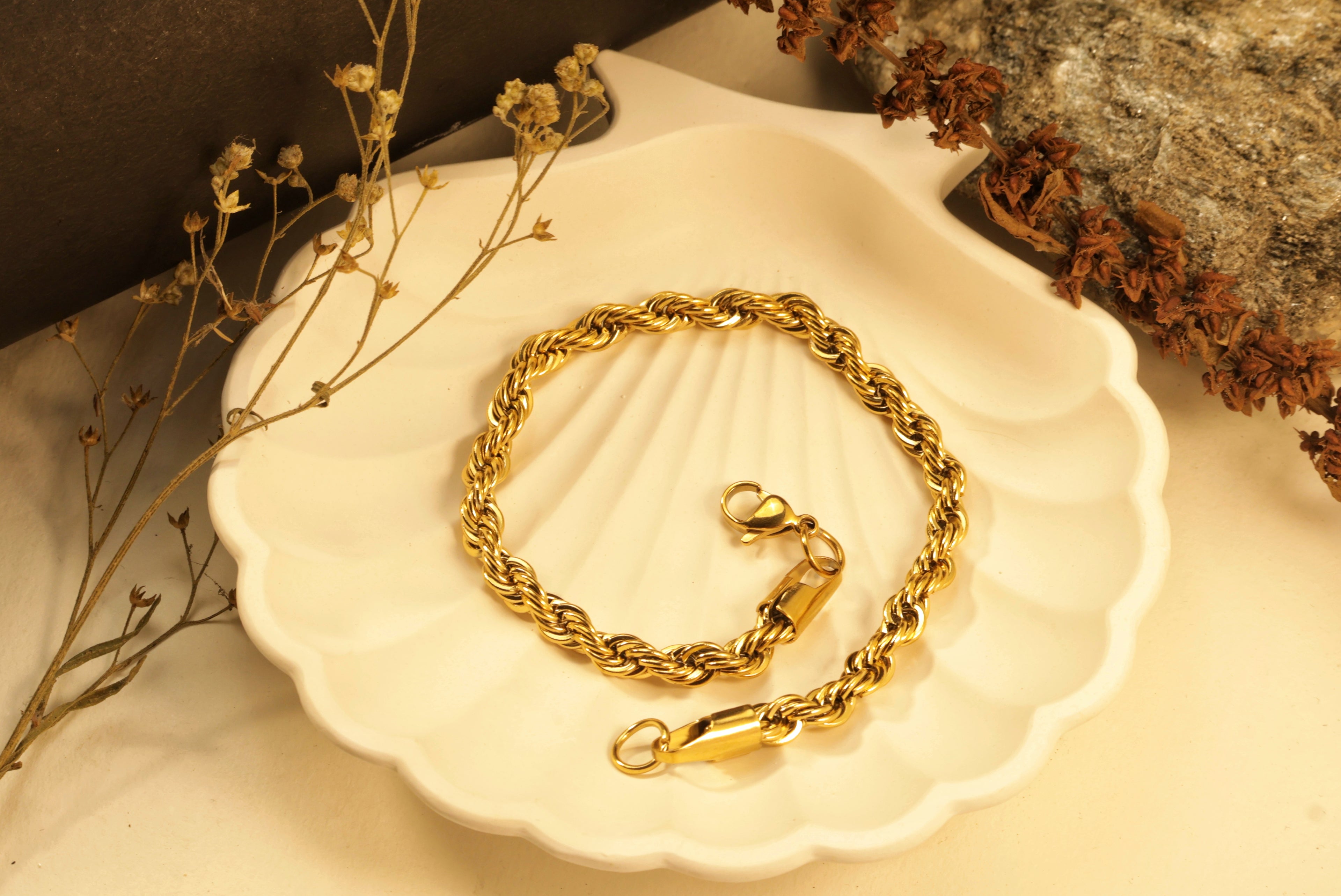 Gold bracelet with a thick, twisted rope-like design on a white plate