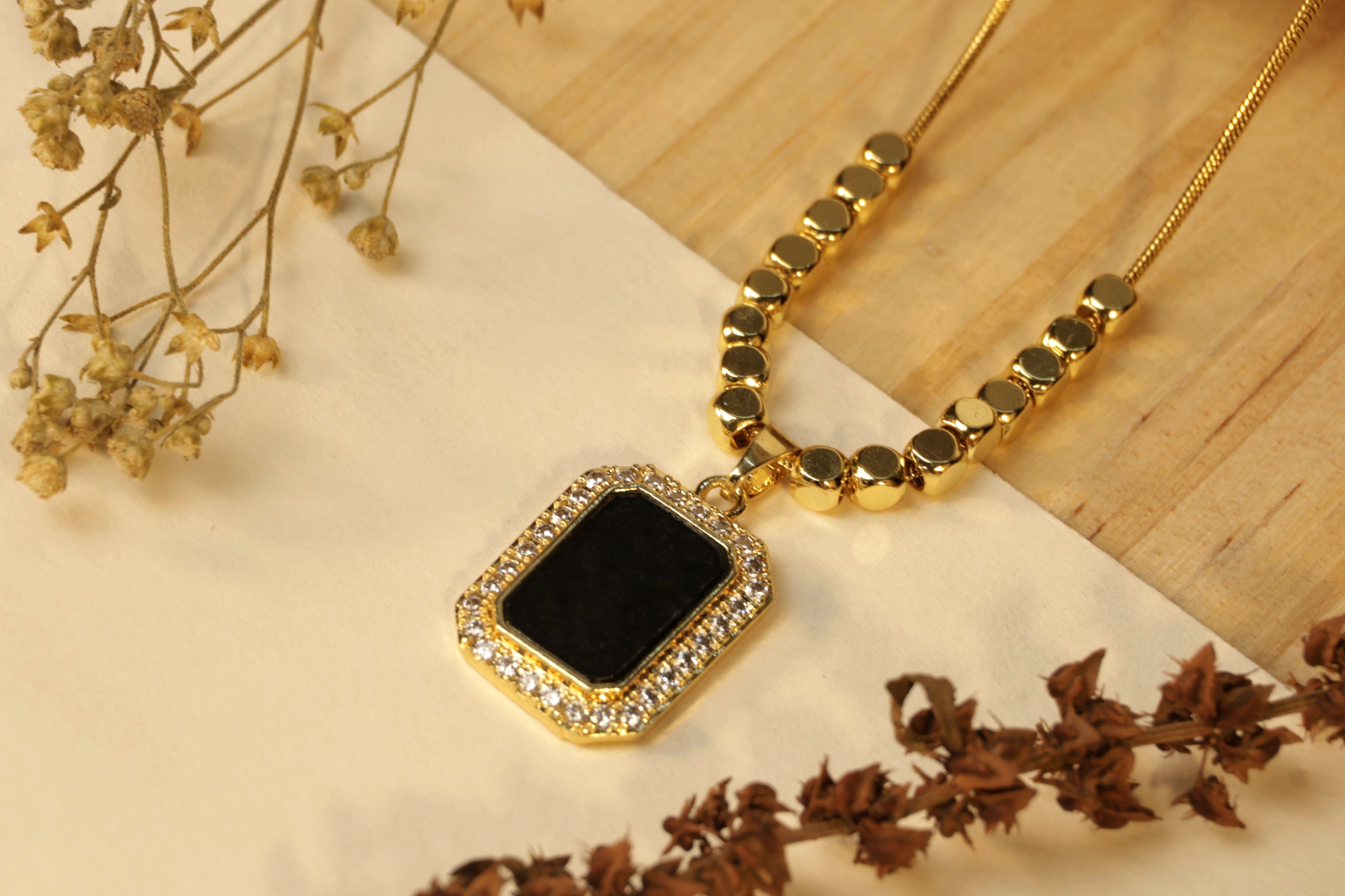 Gold necklace with a square black pendant.