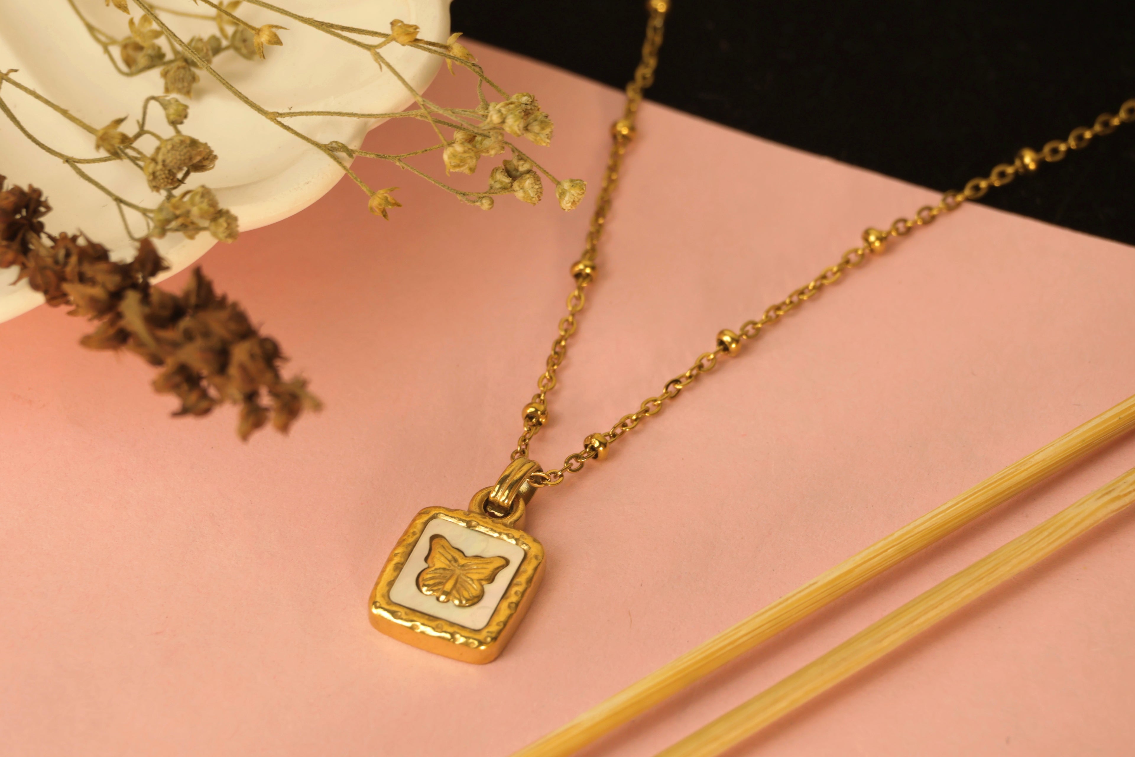 Gold necklace with a square pendant featuring a pearl on a delicate beaded chain.
